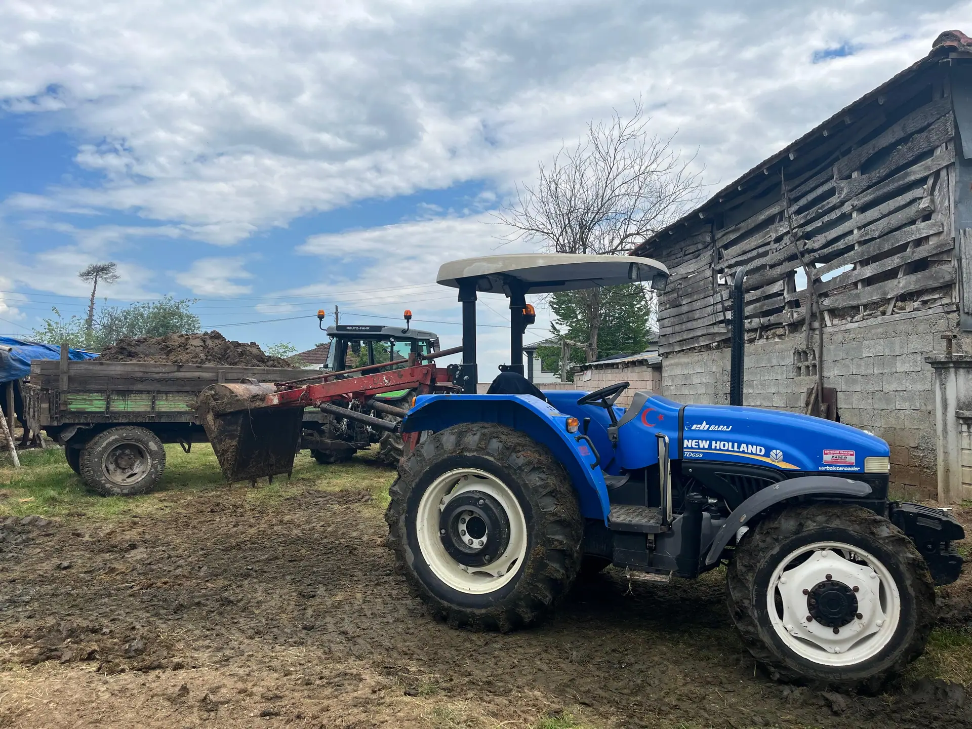 Çiftlik avlusunda römorkuyla çalışan mavi New Holland traktör